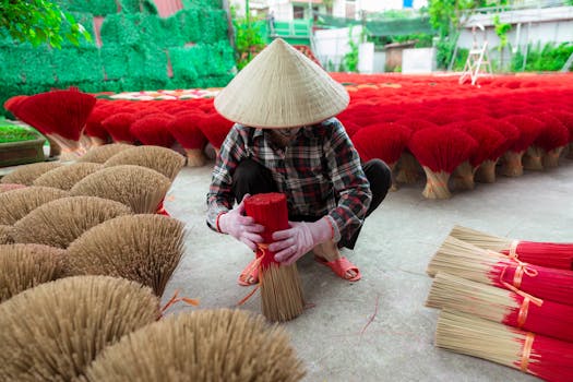 A traditional Vietnamese worker crafting incense outdoors, surrounded by bundles.