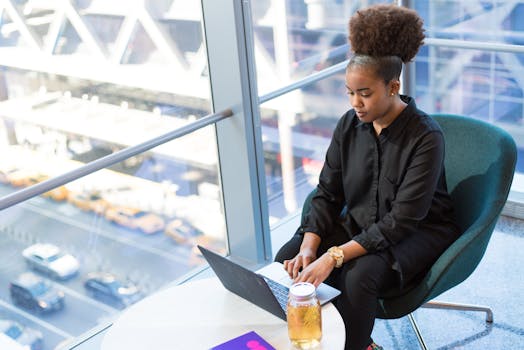 African American woman working on a laptop in a modern office setting, emphasizing professional and technology themes.