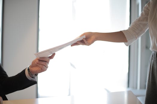 Close-up of hands exchanging documents in a business setting indoors.