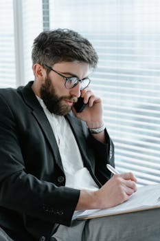 Focused businessman in office, analyzing documents while on a phone call.